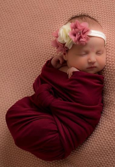 sleeping newborn girl in a floral headband on a pink background
